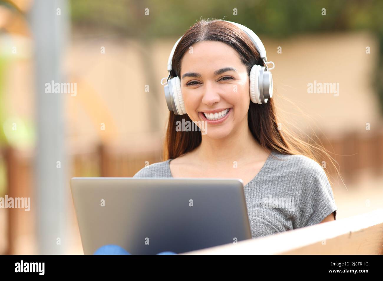 Il ritratto della vista frontale di una donna felice con cuffie wireless e notebook ti guarda Foto Stock