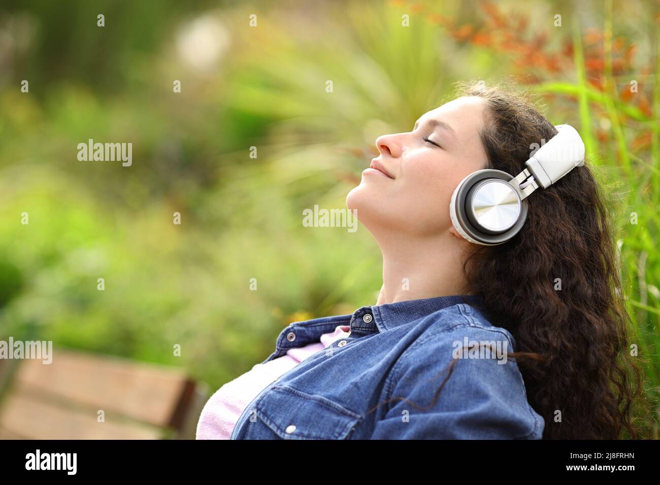 Ritratto laterale di una donna che si rilassa ascoltando la musica con le cuffie in un parco Foto Stock