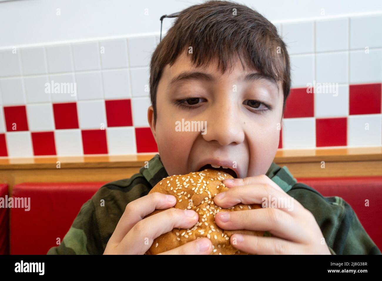 Un ragazzo che prende un boccone da un hamburger in un ristorante fast food Foto Stock