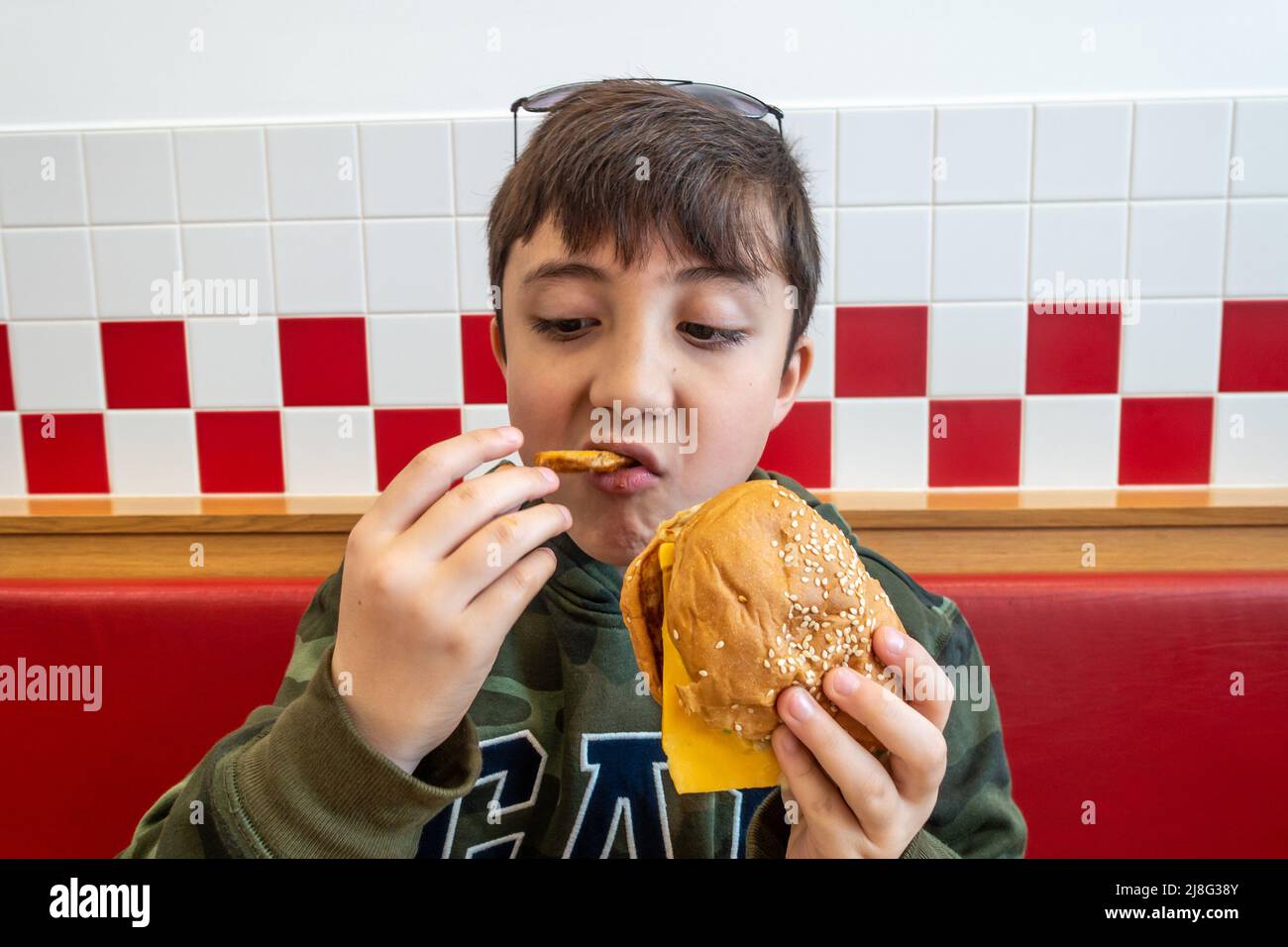 Un ragazzo che mangia hamburger e patatine fritte in un ristorante fast food Foto Stock