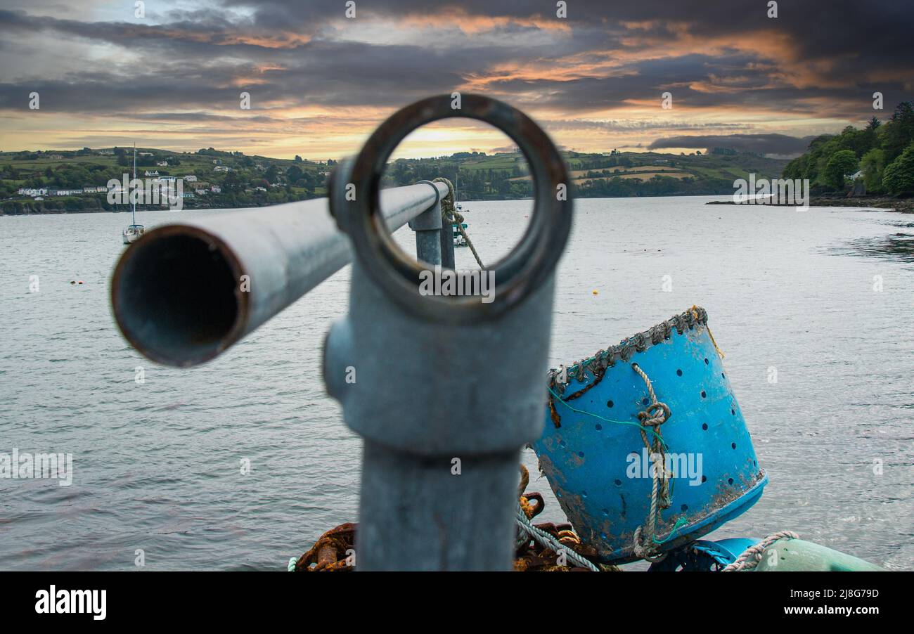 Corda legata alla barriera di sicurezza vista attraverso il foro con nuvole tempesta raccolta. Glandore Harbour, West Cork, Irlanda Foto Stock