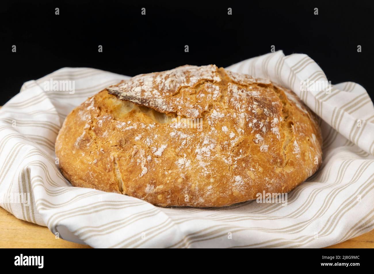 Pane fatto in casa. Pane rotondo appena sfornato su un fondo di legno, messo su un asciugamano di colore chiaro. Foto Stock