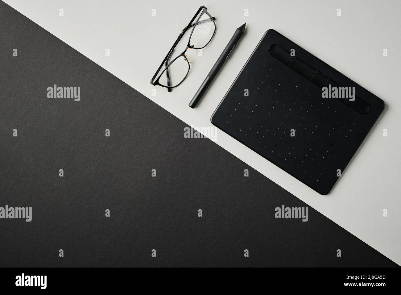 Flatlay di tavoletta grafica, stilo e occhiali su scrivania grigia con parte nera e copyspace per il testo o la pubblicità Foto Stock