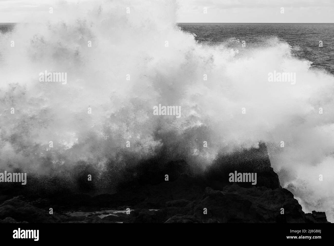 Le onde potenti dell'Oceano Atlantico si infrangono sulle scogliere vulcaniche di Los Hervideros a Lanzarote, Isole Canarie, Spagna, bianco e nero Foto Stock