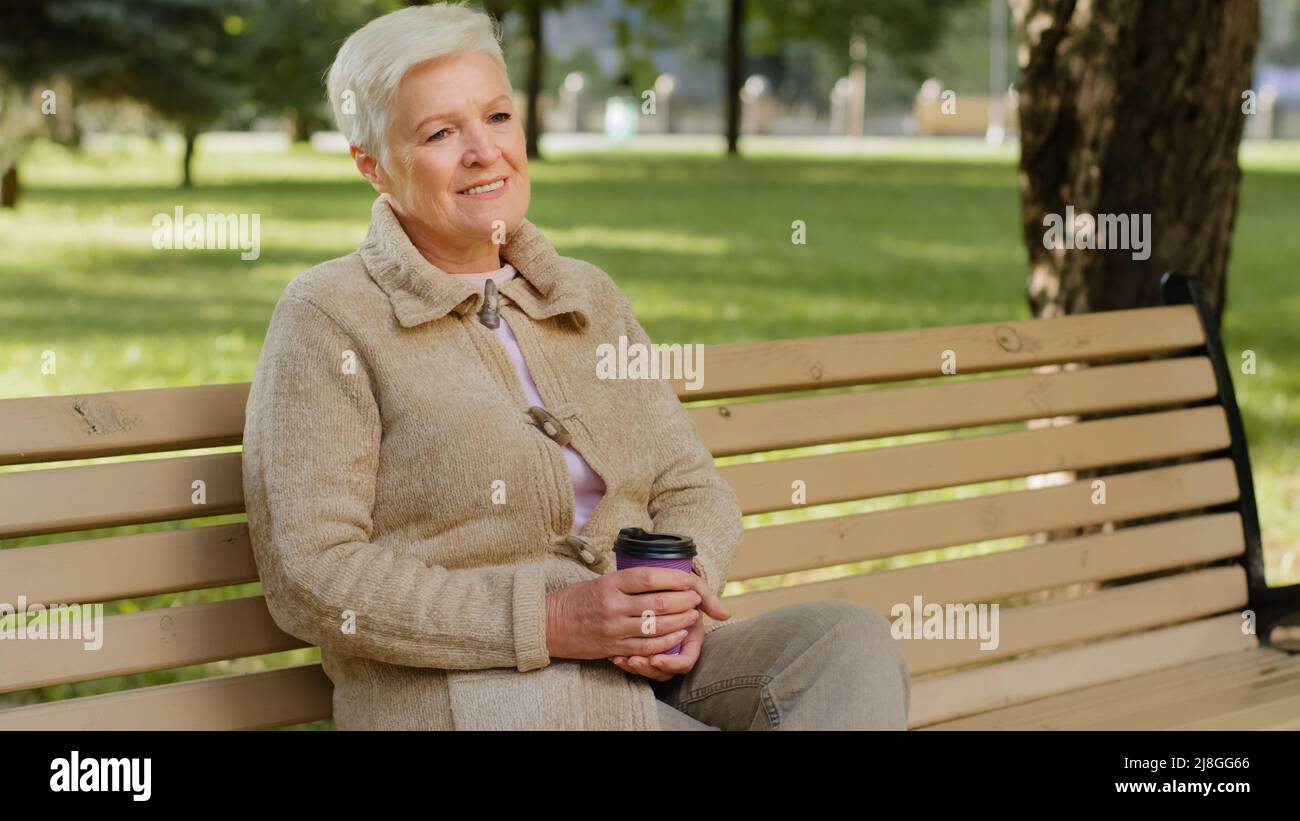 Volto rugoso di 60s felice anziano donna all'aperto in parco guardando da parte avendo ampio sorriso, impianti dentali e protesi soddisfatto ritratto cliente Foto Stock