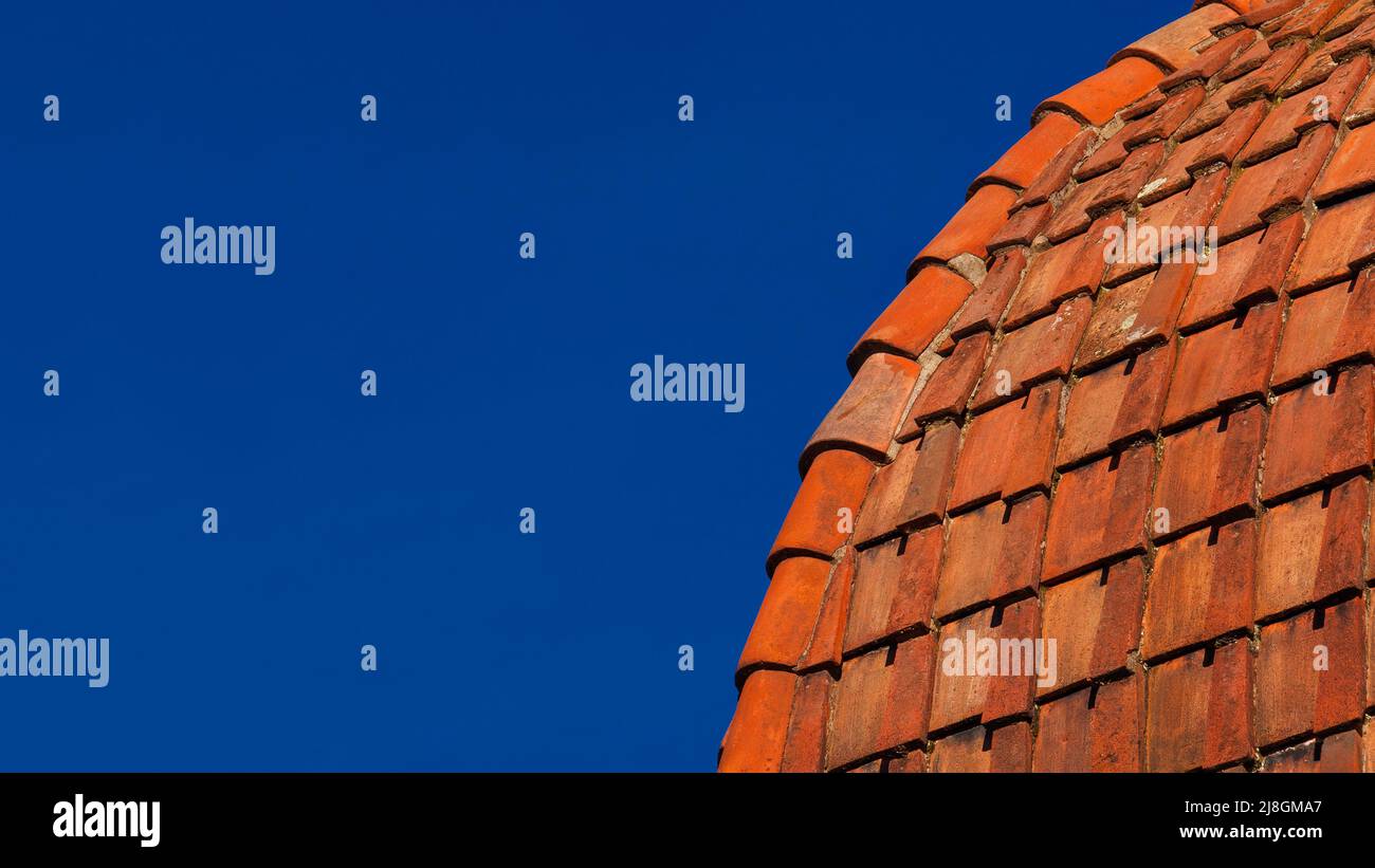 Vecchie tegole rosse e arancioni su una cupola e cielo blu come sfondo (con spazio copia) Foto Stock