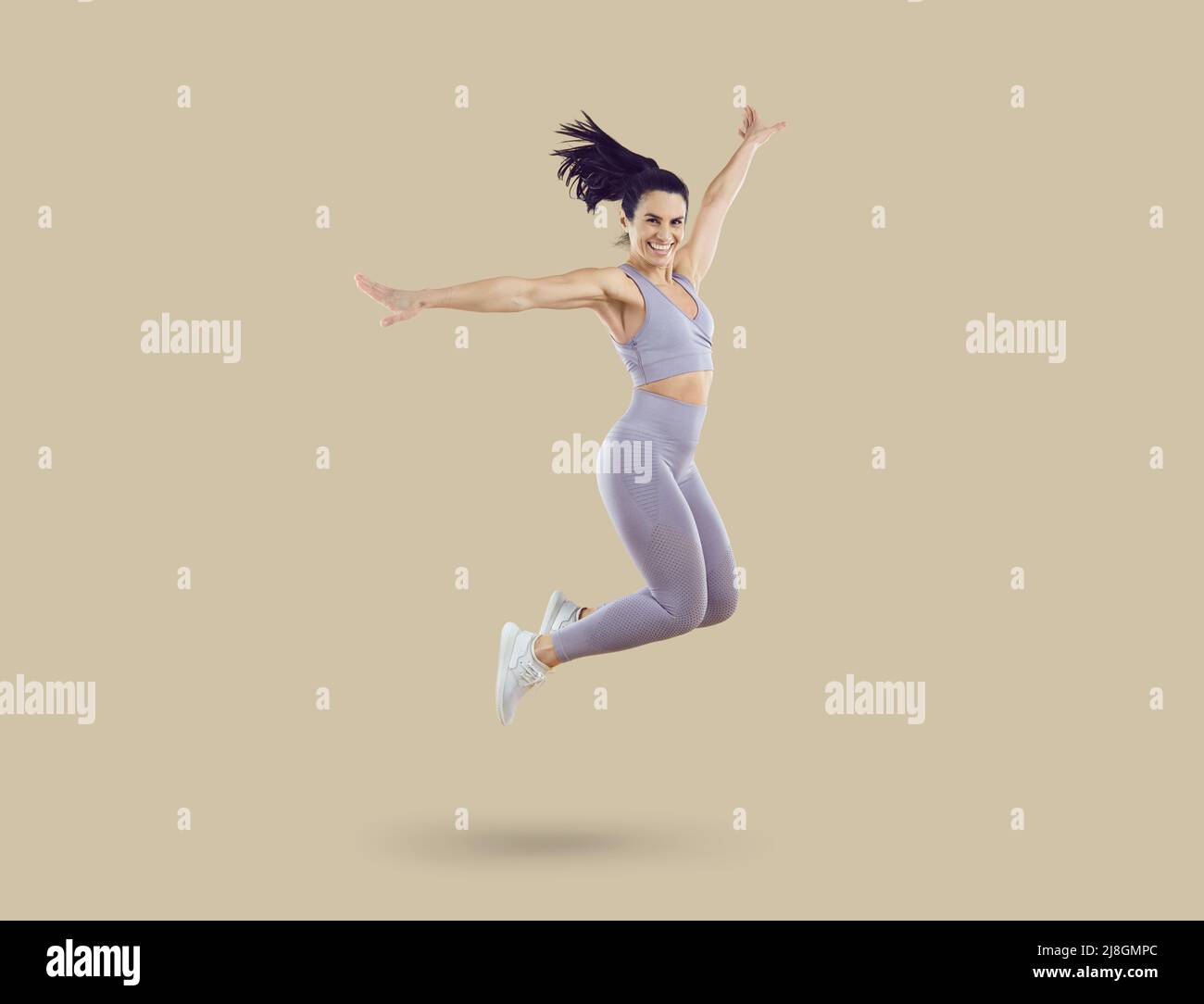 Felice bella donna sportiva in abbigliamento sportivo saltando su sfondo beige studio Foto Stock