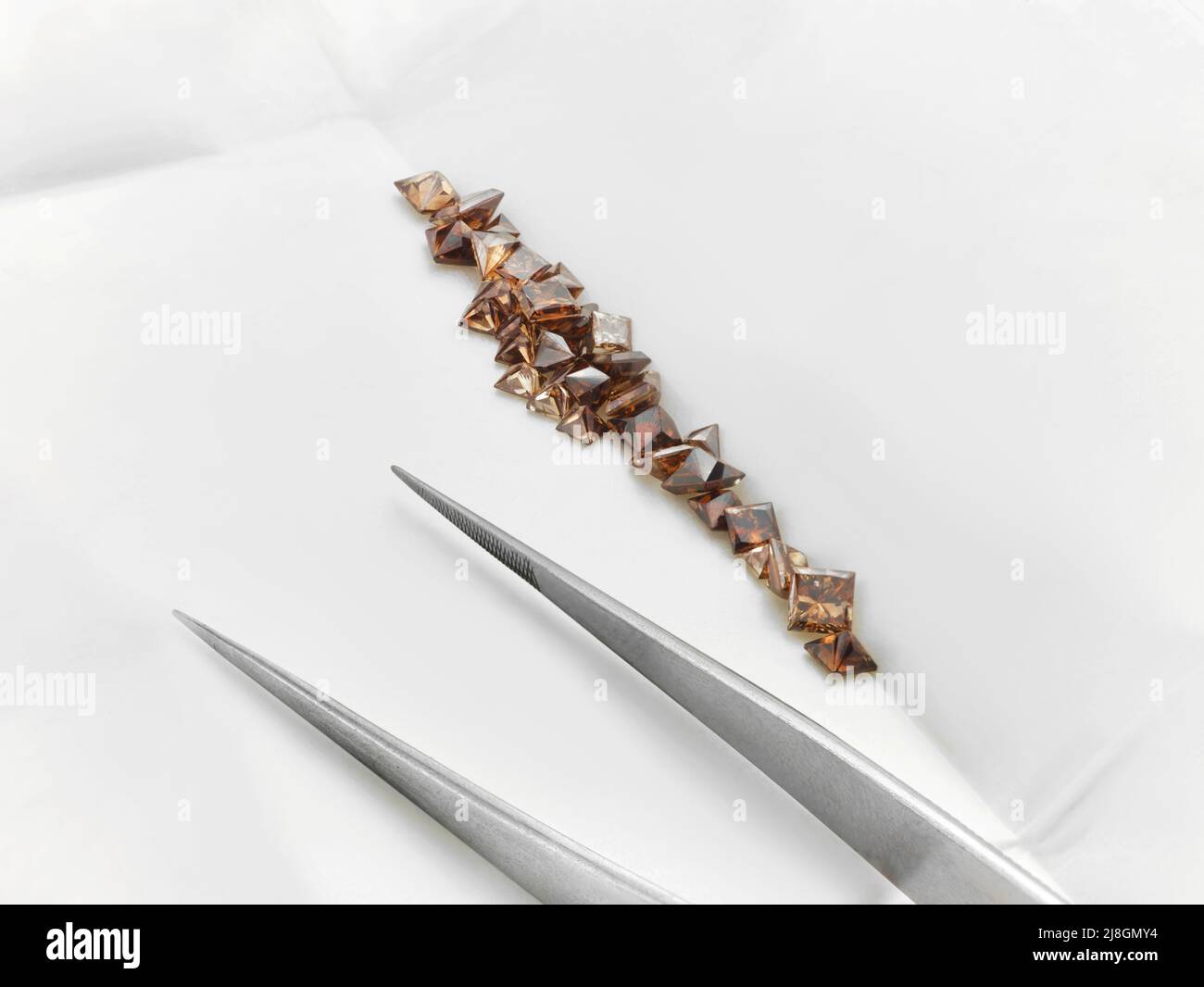 Diamanti di cioccolato. Pacchetto Brown Princess Diamonds con pinzette su sfondo bianco. Foto Stock