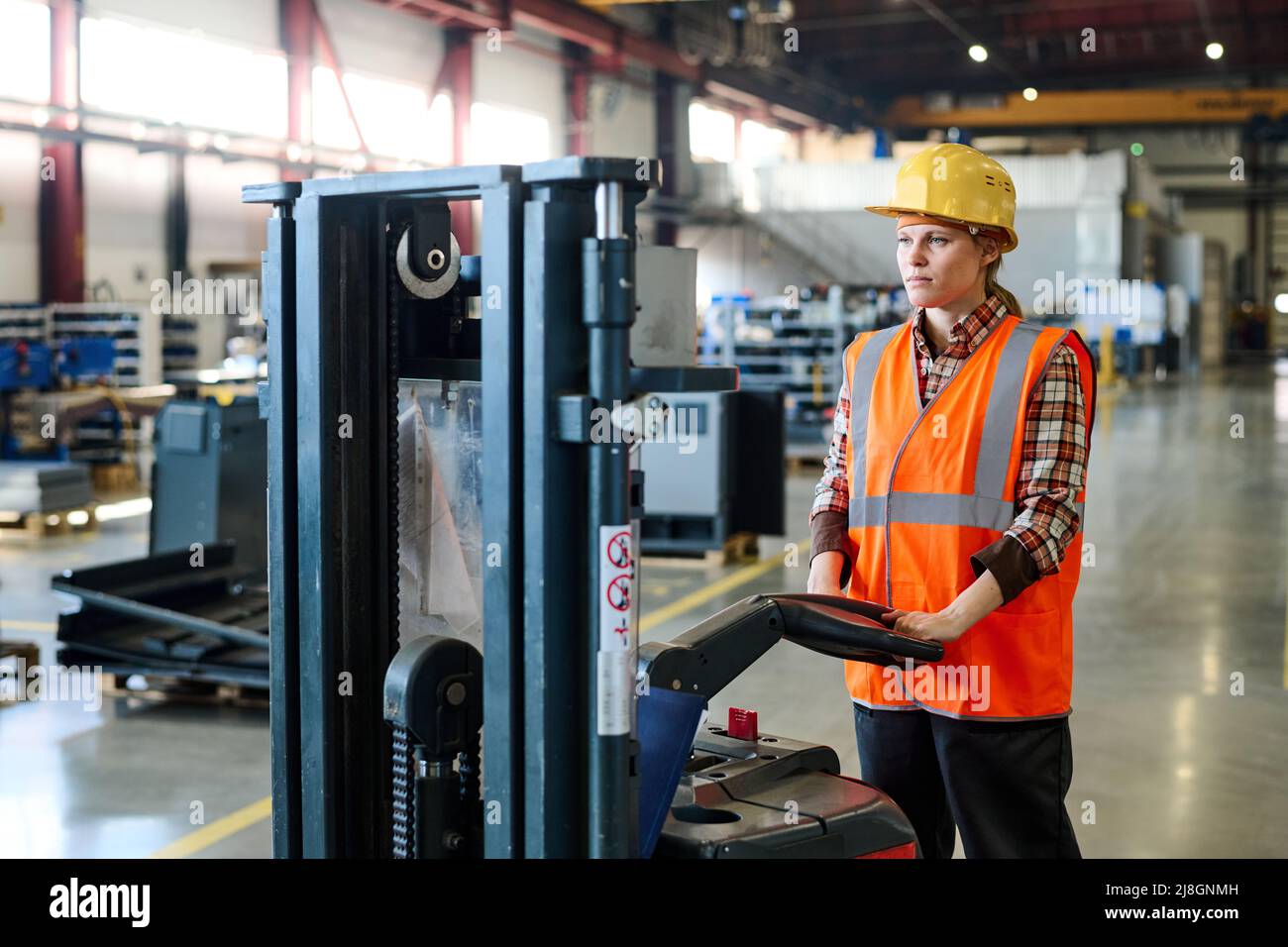 Giovane specialista di grandi fabbriche moderne che spinge il carrello lungo una corsia larga mentre si sposta in avanti in officina contro le attrezzature industriali Foto Stock