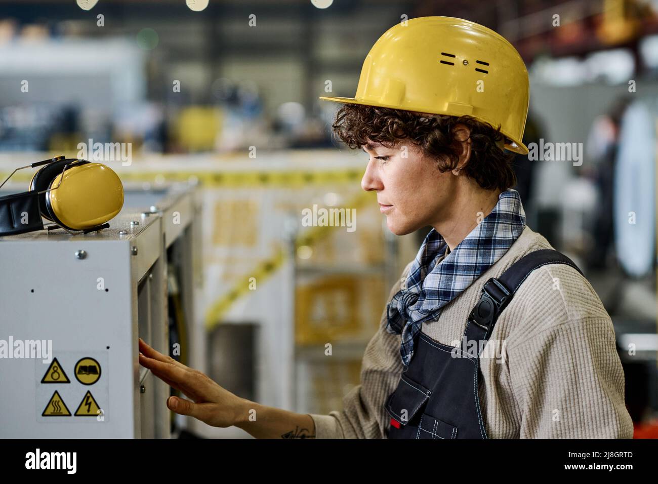 Giovane ingegnere o tecnico di abbigliamento da lavoro e casco protettivo che controlla attrezzature industriali o macchine mentre lavora in fabbrica Foto Stock