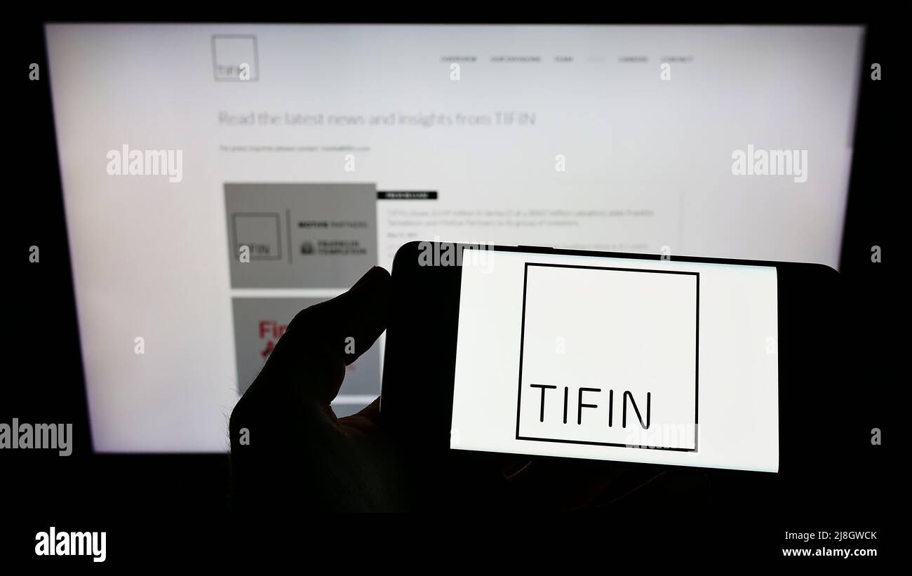 Persona che detiene il telefono cellulare con il logo della società americana di consulenza per gli investimenti Tifin LLC sullo schermo di fronte alla pagina web. Mettere a fuoco sul display del telefono. Foto Stock