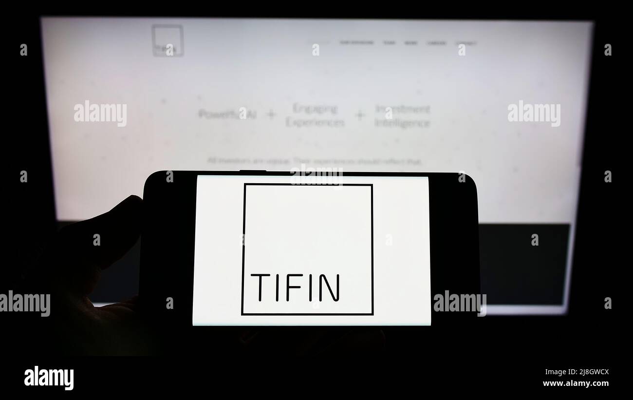 Persona che detiene il cellulare con il logo della società di consulenza di investimento statunitense Tifin LLC sullo schermo di fronte al sito web aziendale. Mettere a fuoco sul display del telefono. Foto Stock