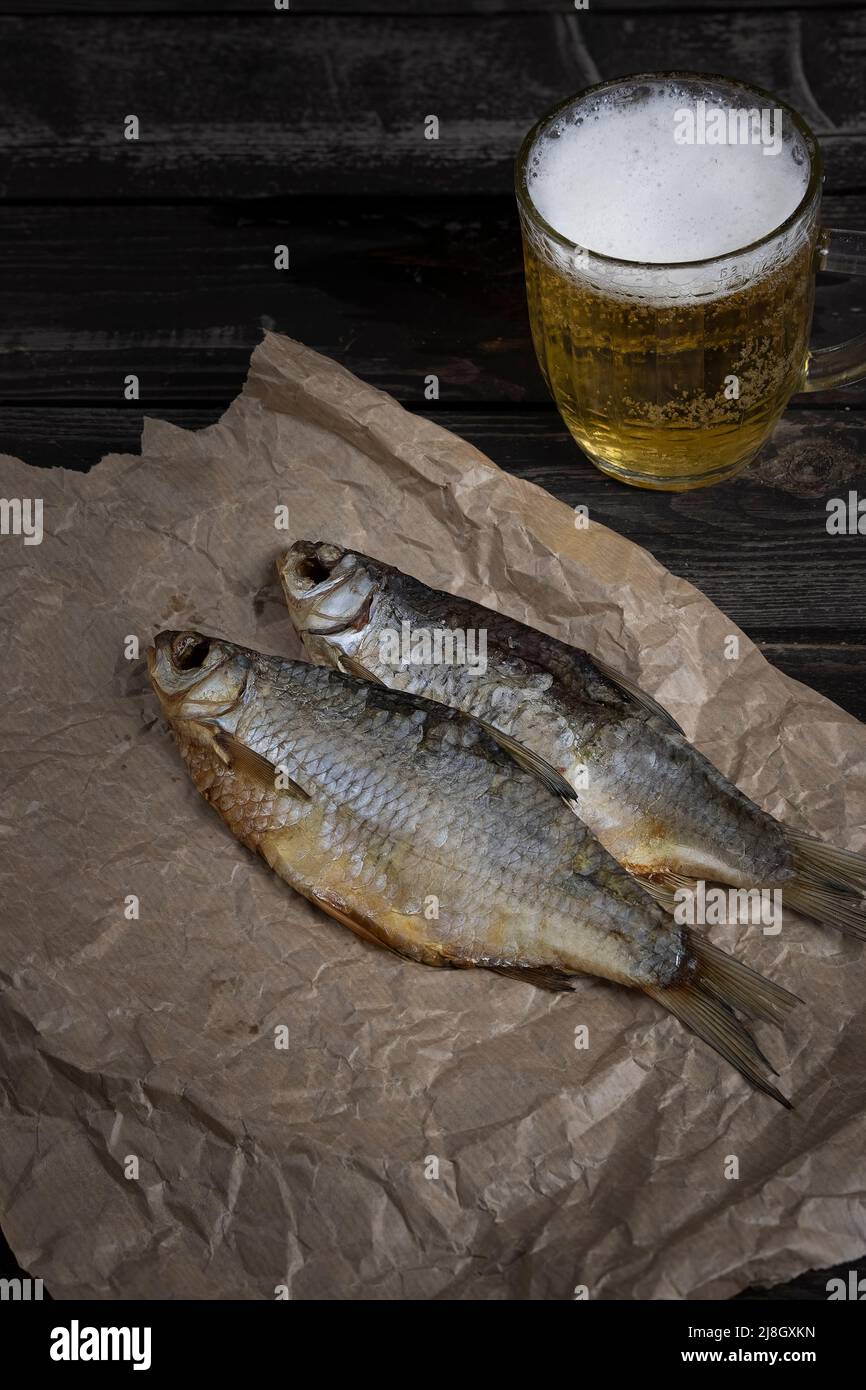 pesce vobla salato e secco con birra ambrata su sfondo di legno scuro con pane sul tavolo, Foto Stock