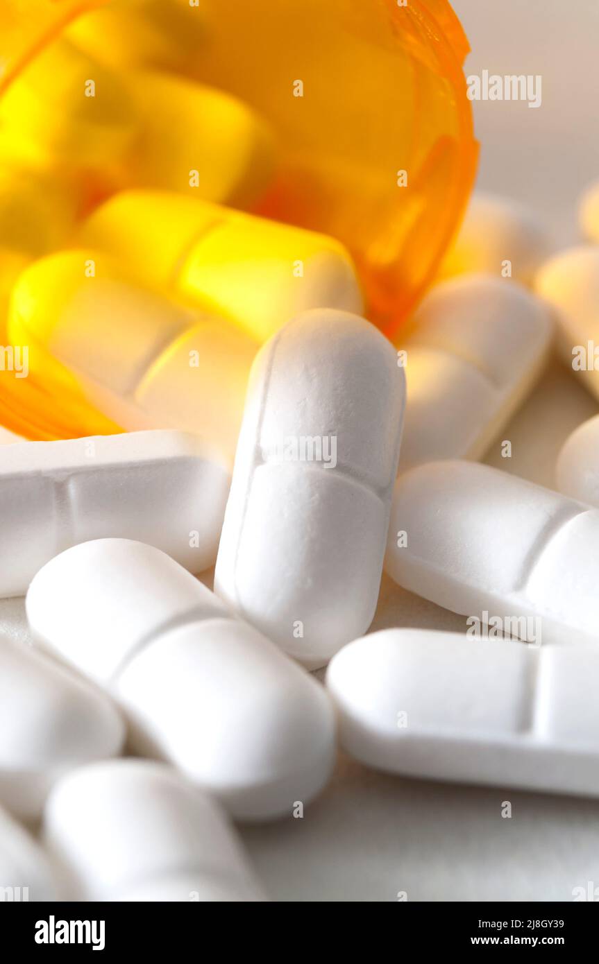 Epidemia di oppioidi, antidolorifici e concetto di abuso di droga con primo piano su una bottiglia di farmaci da prescrizione e pillole di idrocodone che cadono da esso su bianco Foto Stock