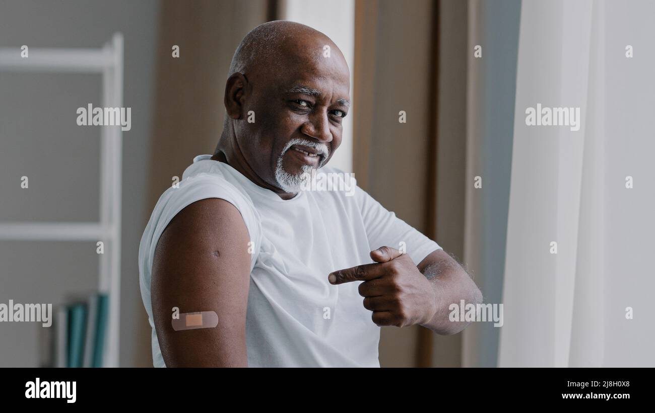 Ritratto africano americano anziano anziano paziente uomo maturo mostra cerotto medico sulla spalla segno di iniezione soddisfatto maschio dopo la vaccinazione con covid Foto Stock