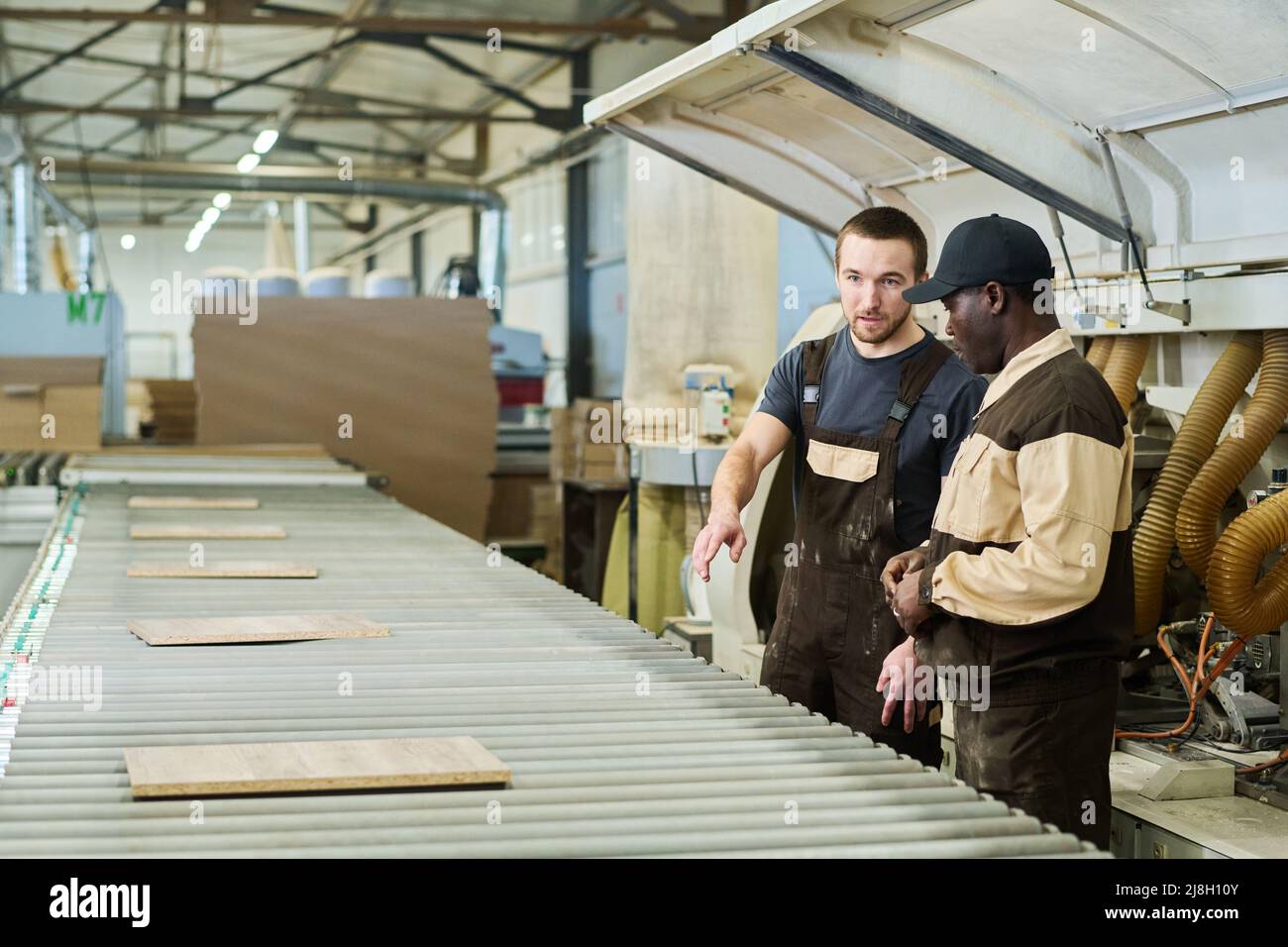 Lavoratore in unibrem discutere la produzione di dettagli con il caposquadra mentre si trova accanto alla macchina in fabbrica Foto Stock