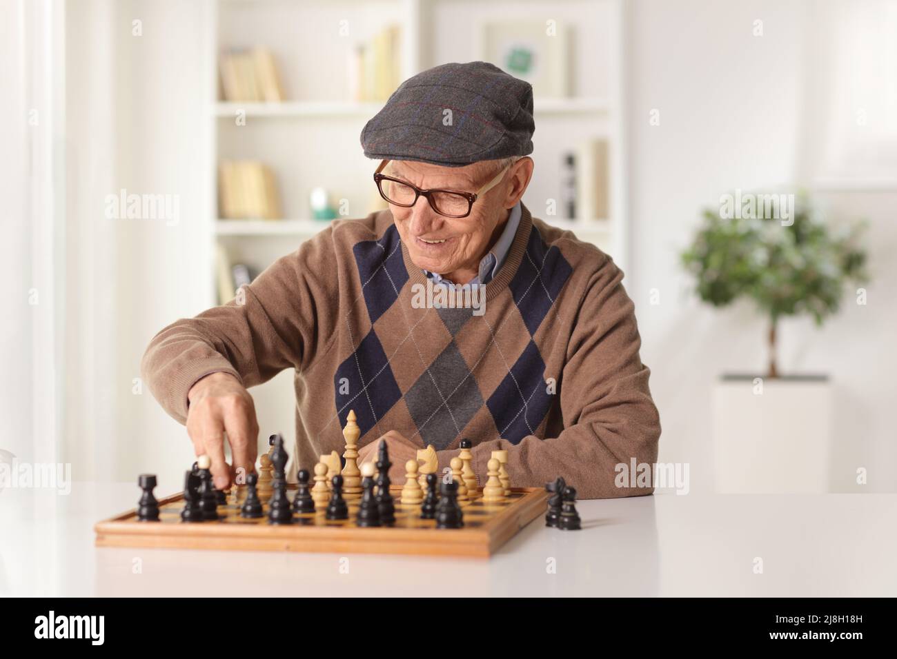 Uomo anziano seduto a casa e giocare a scacchi Foto Stock