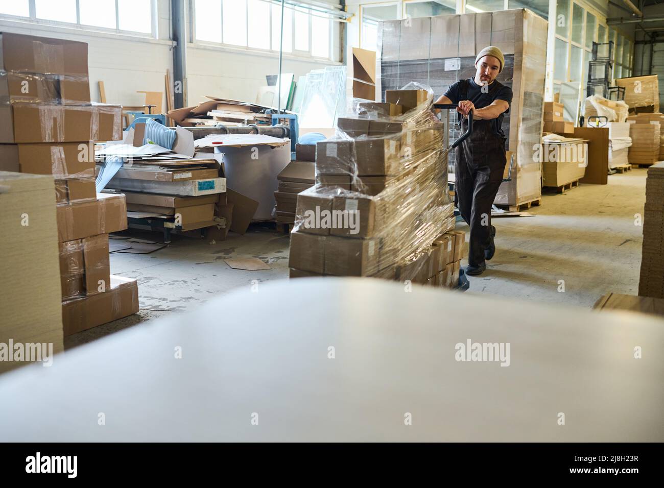 Carrello da trasporto per giovani lavoratori con scatole di cartone imballate lungo il magazzino Foto Stock