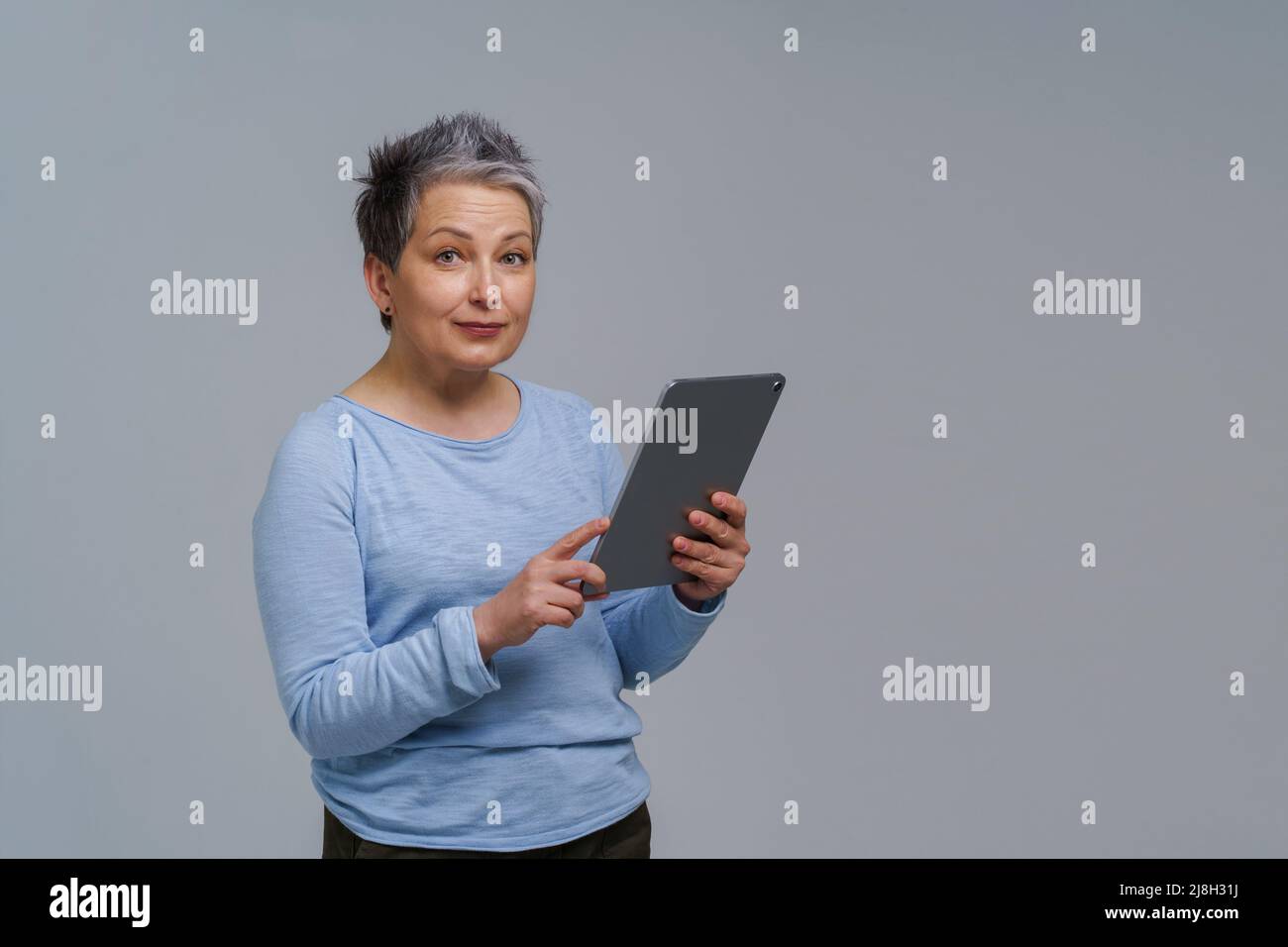 Meravigliosa donna matura 50s capelli grigi con tablet digitale che funziona o controlla sui social media. Bella donna in blusa blu isolato su bianco. Persone anziane e tecnologie. Immagine a toni. Foto Stock