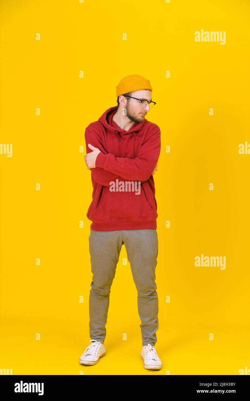 Giovane uomo in stile casual in occhiali in posa guardando lateralmente su sfondo giallo con un braccio ripiegato. Elegante look casual da uomo hipster dal bearded elegante. Ragazzo premuroso su sfondo giallo. Foto Stock