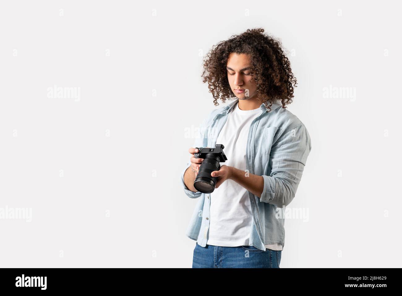 Il giovane uomo con capelli ricci sta tenendo una macchina fotografica sulla sua mano. Concetto di hobby e fotografia. Foto di alta qualità Foto Stock