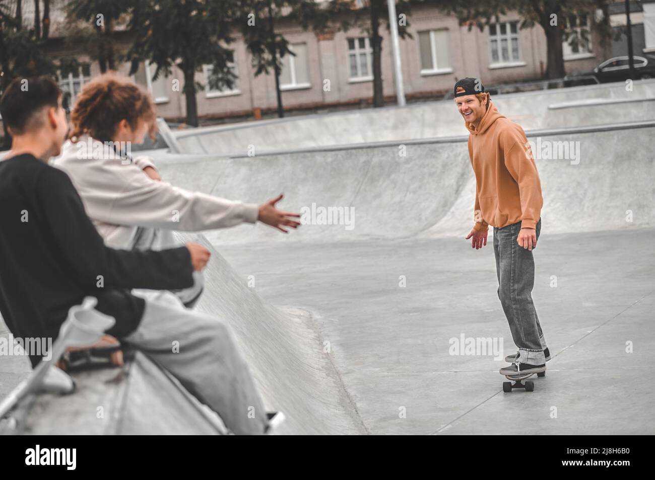 Ragazzo sullo skateboard che guarda gli amici che si siedono gesturing Foto Stock