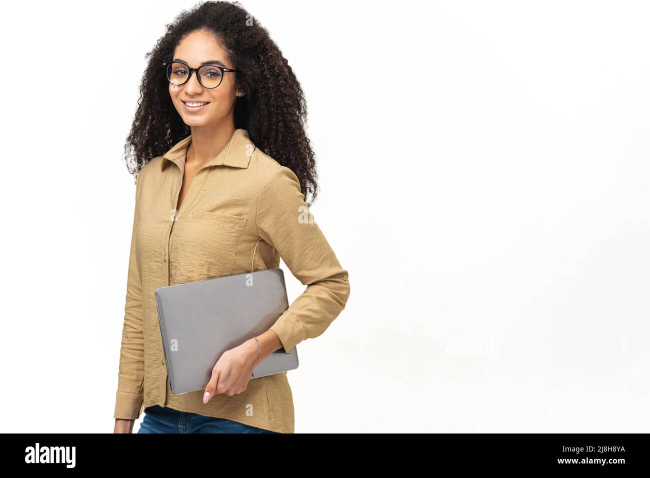 Giovane afroamericana con acconciatura afrofroche indossa abbigliamento casual elegante e occhiali eleganti in piedi isolato su bianco, portando computer portatile, sorridente, dipendente di ufficio femminile, studente Foto Stock
