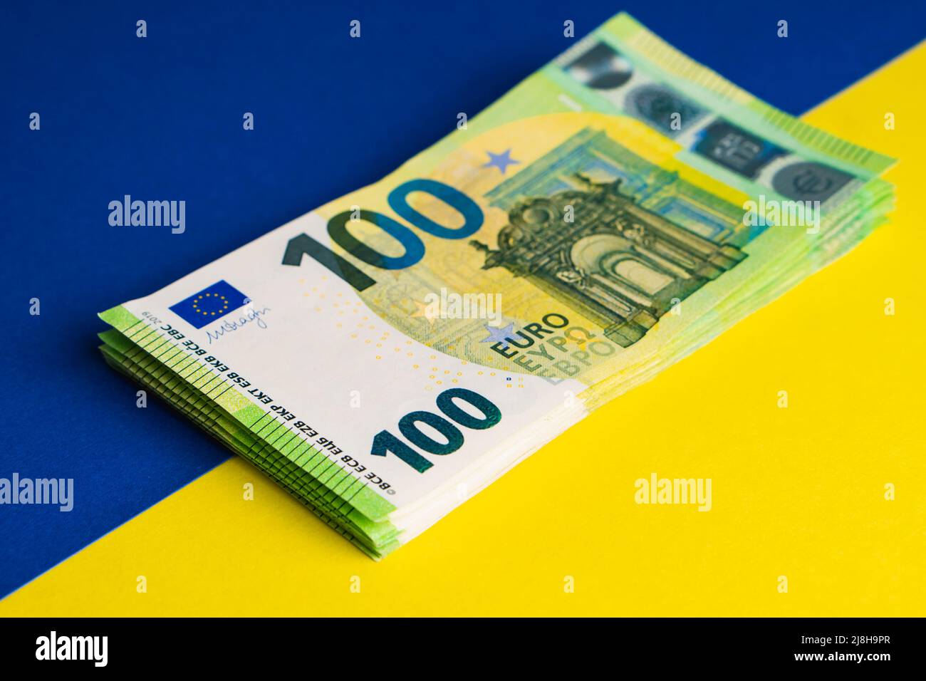 Pila di cento banconote in euro sulla bandiera Ucraina. Aiuti finanziari dall'Europa all'Ucraina concetto Foto Stock