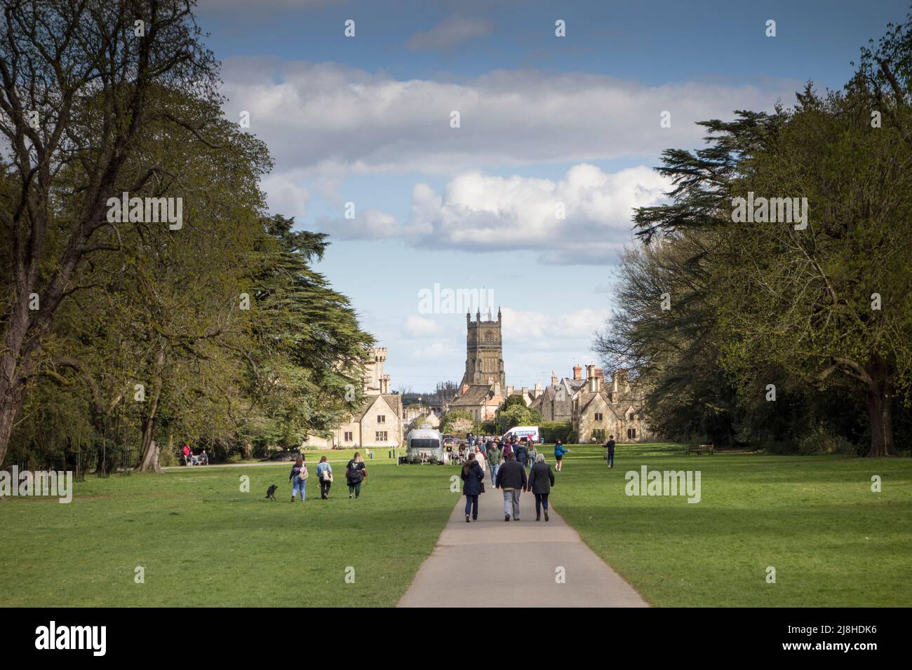 Persone che camminano a terra del Cirencester Park con la chiesa di San Giovanni Battista in background, Gloucestershire, Regno Unito Foto Stock