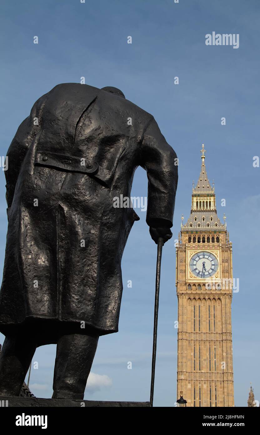 Retro della statua della scultura in bronzo di Sir Winston Churchill con bastone da passeggio che guarda verso la regina Elizabeth Tower e il Big ben nella piazza del Parlamento Foto Stock