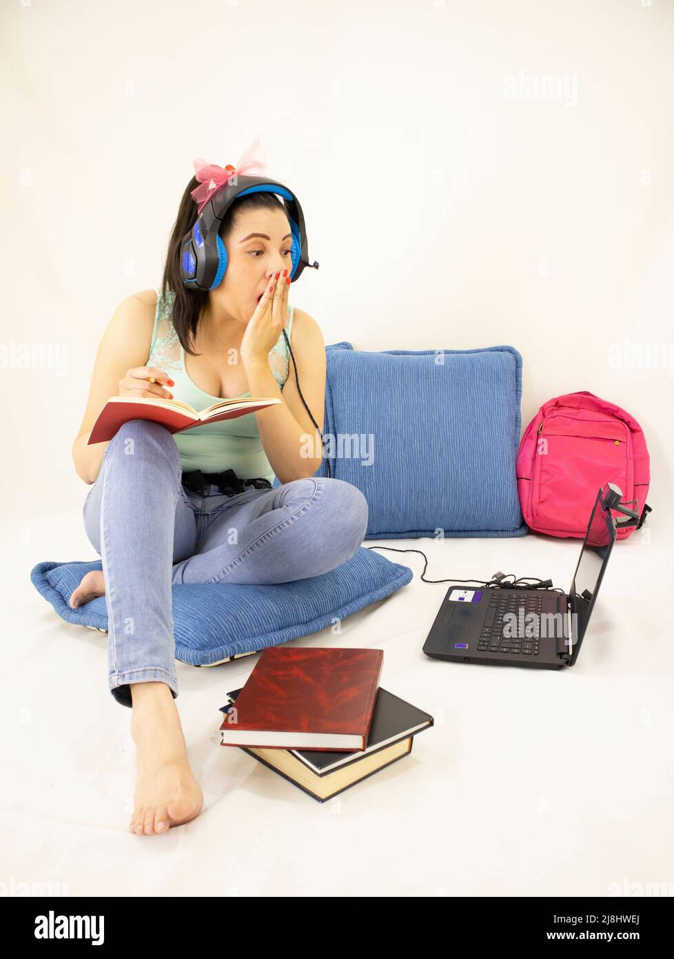 annoiato giovane studentessa donna studiare online con cuffie, libri, web camera, computer e zaino Foto Stock