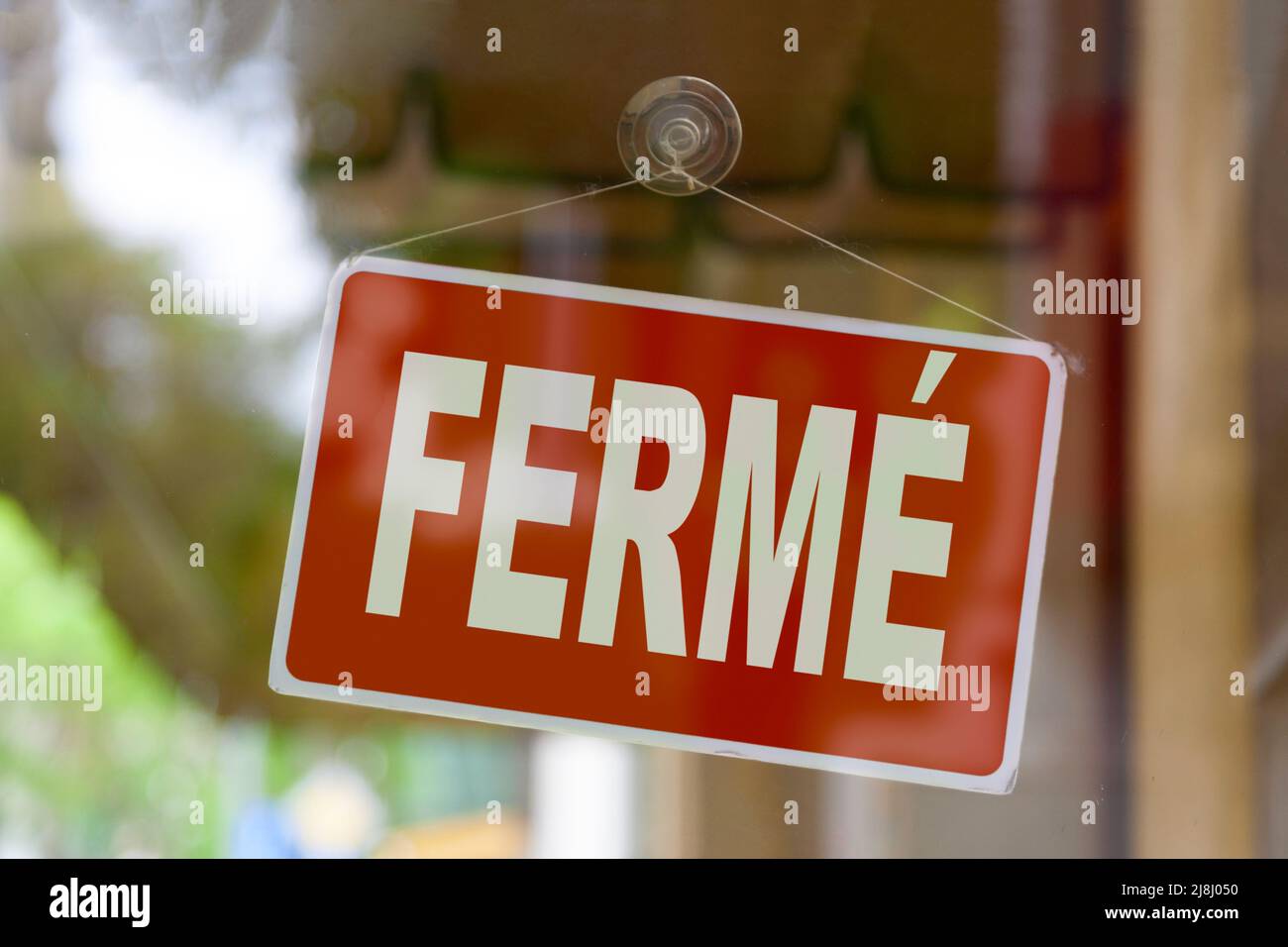 Primo piano su un segno rosso nella finestra di un negozio che visualizza il messaggio in francese - Fermé - significato in inglese - chiuso -. Foto Stock