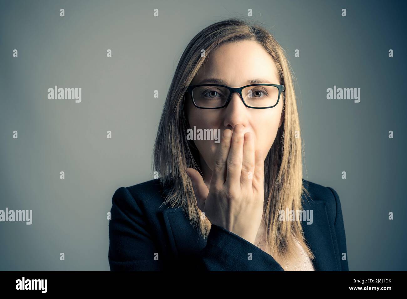 ritratto di donna che ricopre la bocca su sfondo grigio Foto Stock