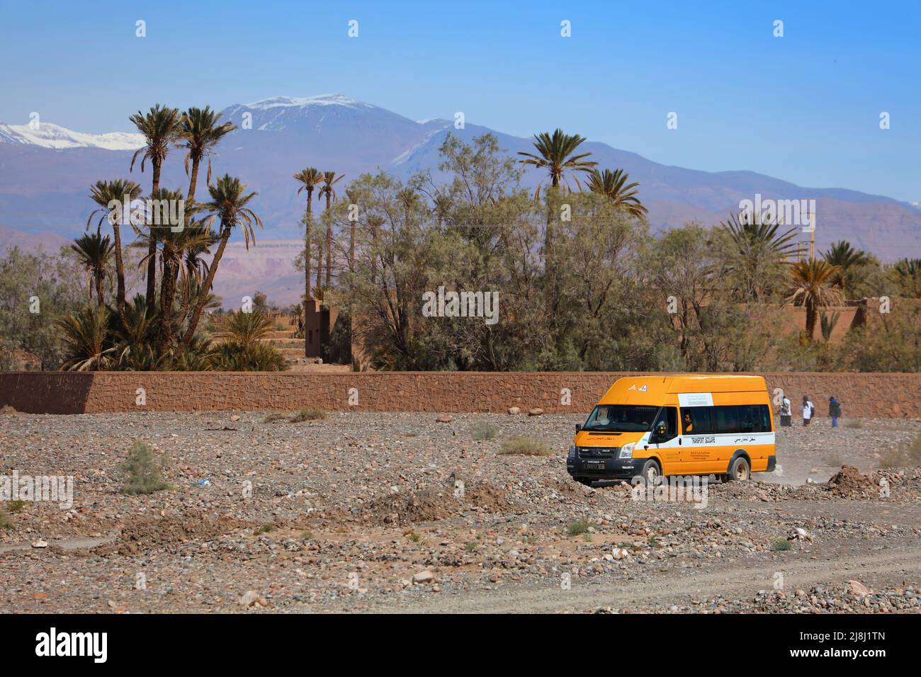 OUARZAZATE, MAROCCO - 18 FEBBRAIO 2022: L'autobus scolastico giallo naviga su strade sterrate in Marocco rurale con montagne dell'Atlante sullo sfondo. È stato finanziato da N Foto Stock