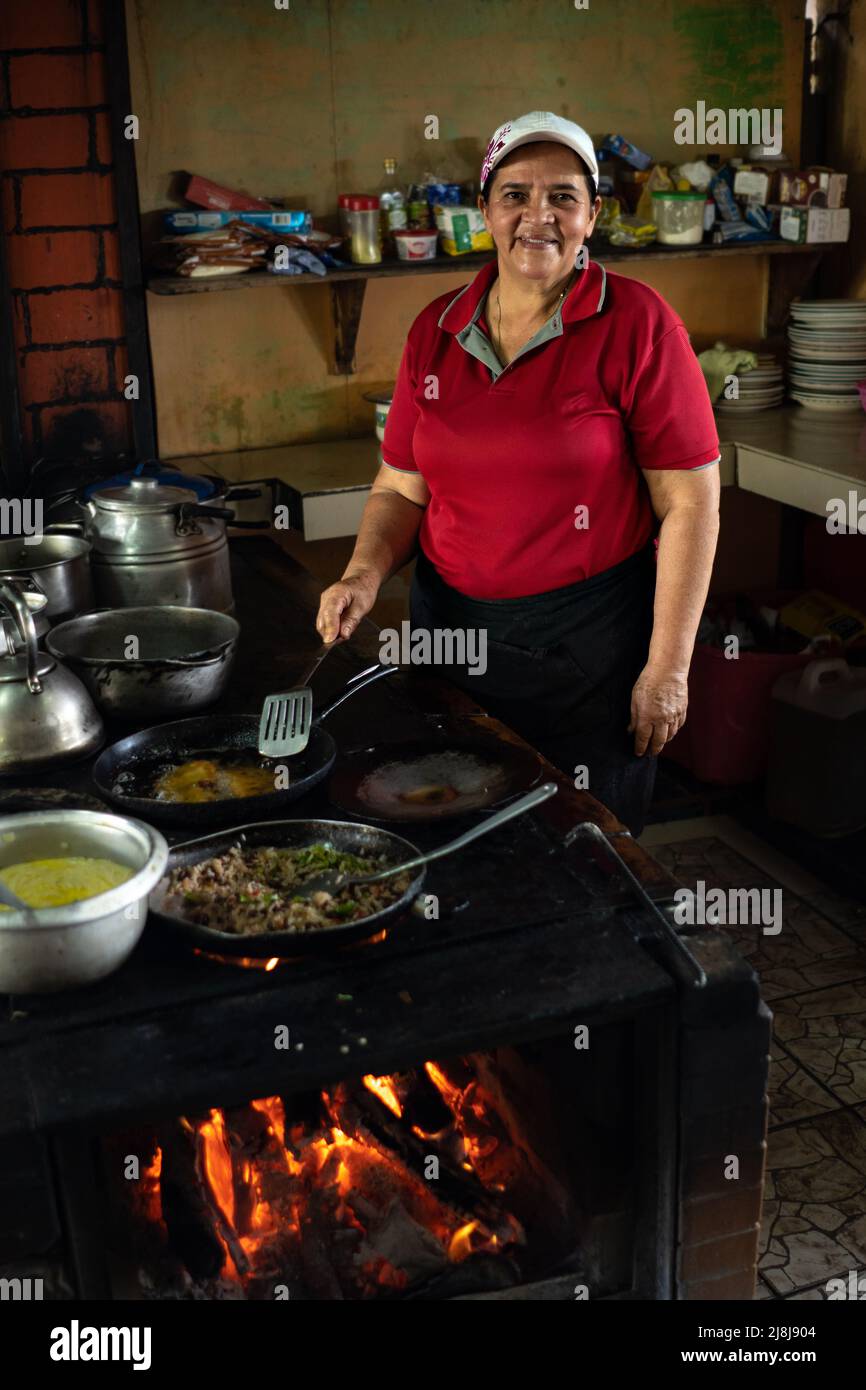 La donna più anziana che cucinava guarda la macchina fotografica e sorride. Foto Stock