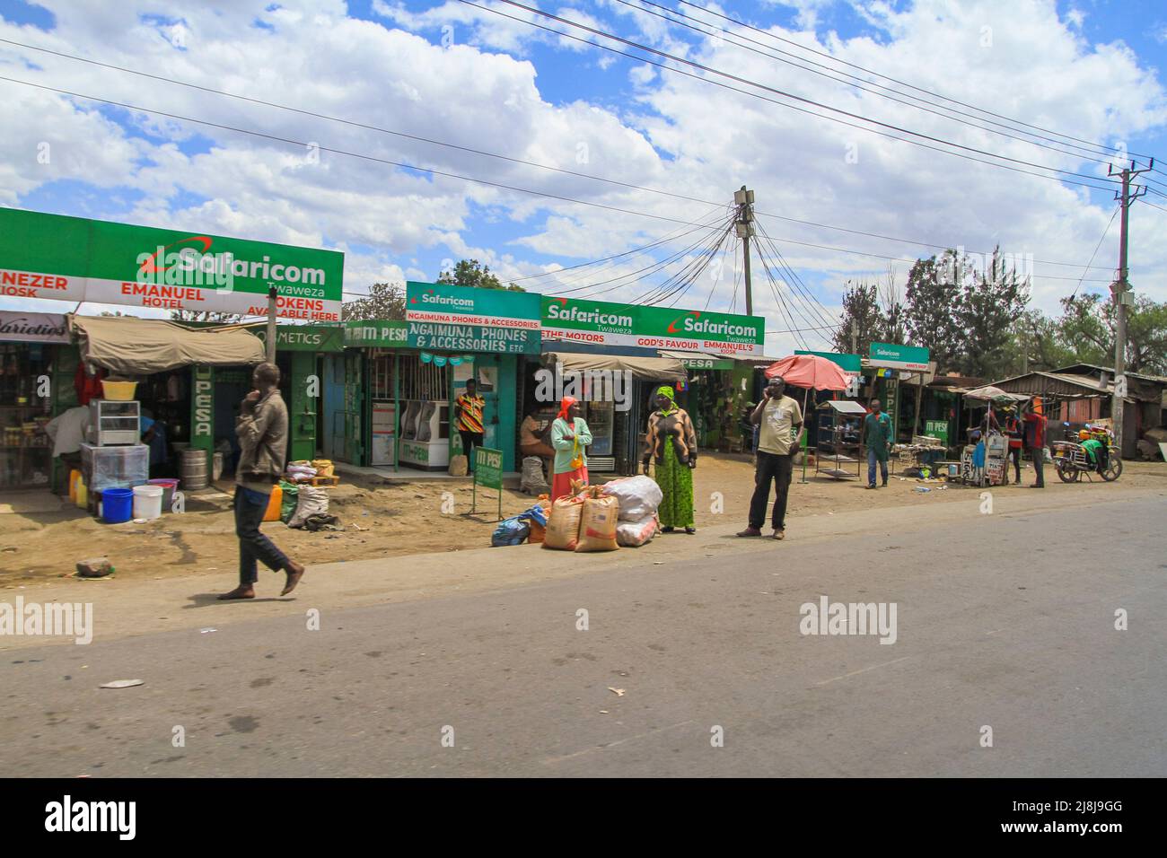 Negozio Safaricom nel villaggio keniota. Uno dei più grandi fornitori di tecnologia mobile internet del Kenya. Gente lungo la strada con piccoli negozi. Kenya, Africa Foto Stock