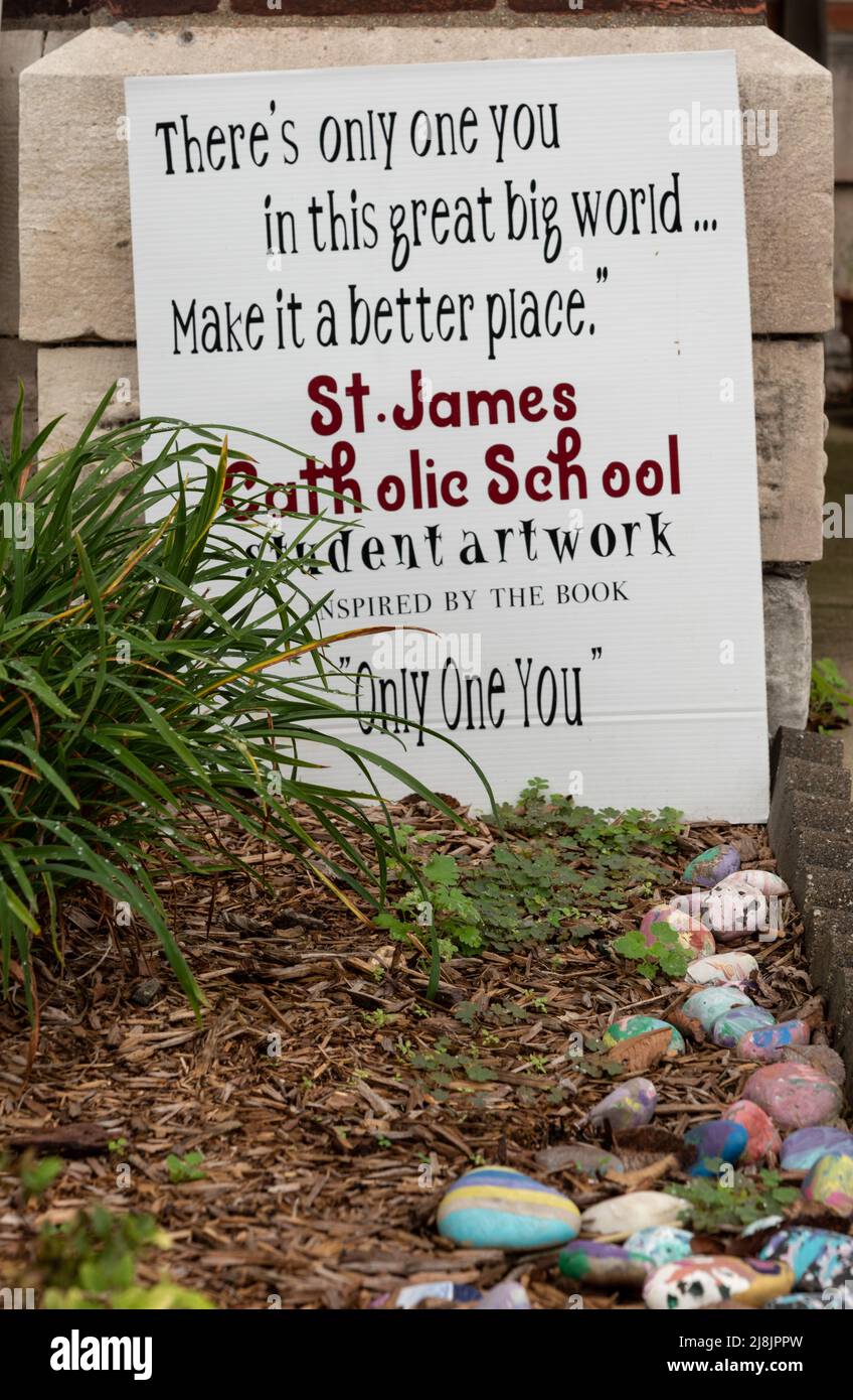 Una linea di rocce dipinte conduce ad un cartello appoggiato contro un muro con parole di incoraggiamento della St James Catholic School, USA. Foto Stock