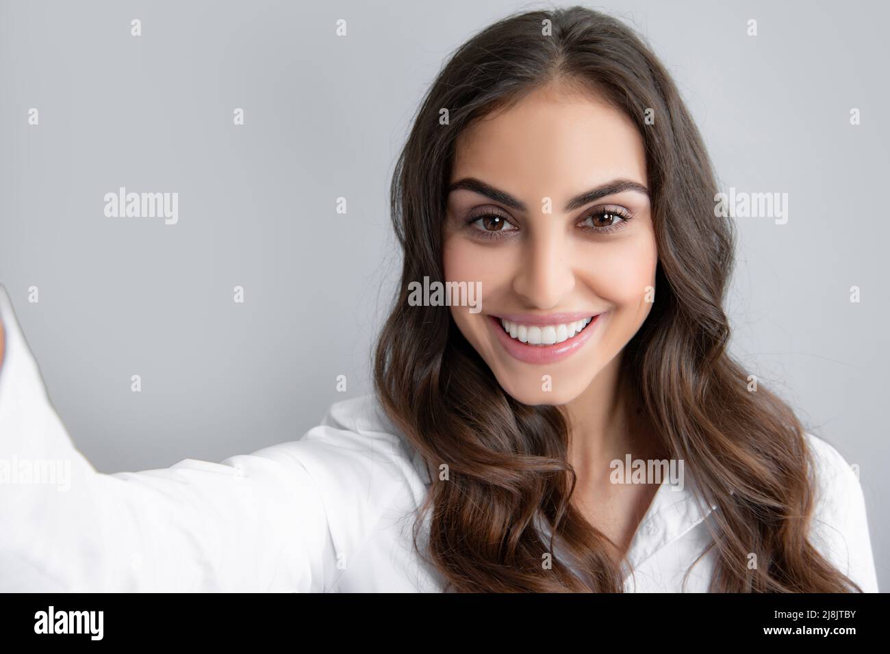 Studio ritratto di bella donna sorridente facendo selfie, fotografandosi su sfondo grigio. Foto Stock