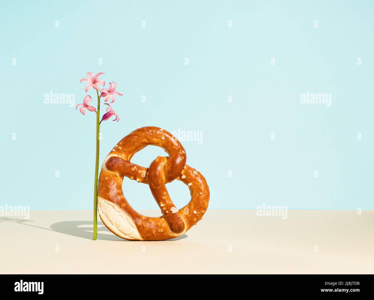 Sacchetto di pane a forma di cuore con semi di sesamo e giacinto rosa su sfondo azzurro. Concetto minimo di cibo. Pasticceria turca tradizionale. Foto Stock