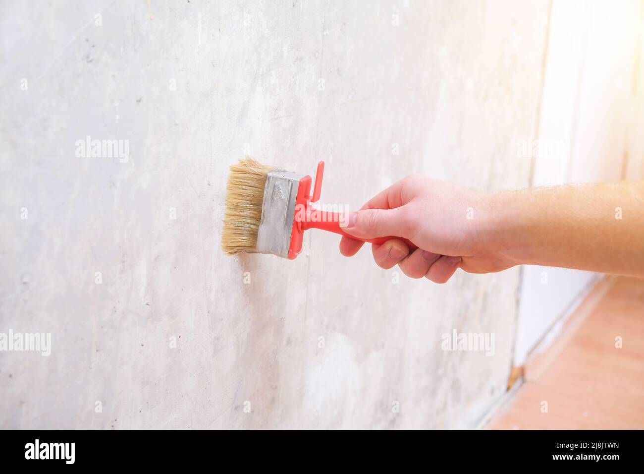 Un uomo applica colla per tappezzeria con un pennello per tappezzeria. Riparazione di una stanza, appartamento, casa. Foto Stock