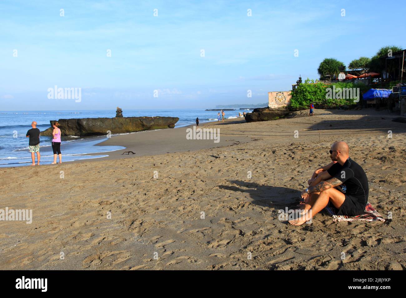 Molti visitatori caucasici seduti e in piedi alla spiaggia di Batu Bolong a Canggu, Bali, Indonesia, mentre guardano i surfisti nell'oceano. Foto Stock