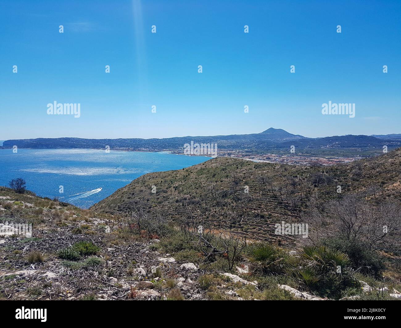 Vista sul paesaggio collinare della costa mediterranea spagnola fino alla striscia costiera di Xavia con alcuni villaggi e montagne all'orizzonte sotto il sole Foto Stock