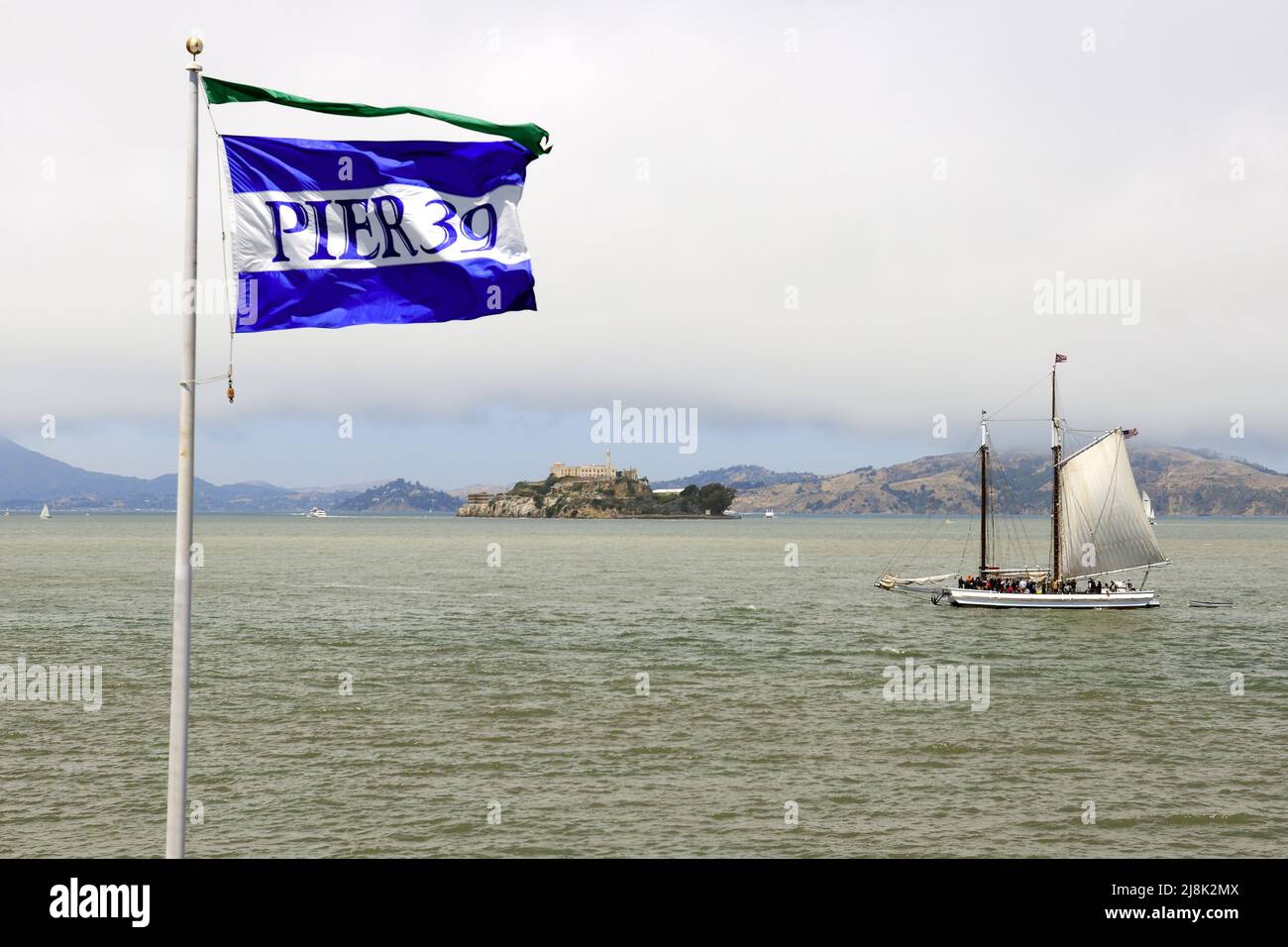 Bandiera del Molo 39 al Fisherman's Wharf e storica nave a vela di fronte all'isola carceraria di Alcatraz, USA, California, San Francisco Foto Stock