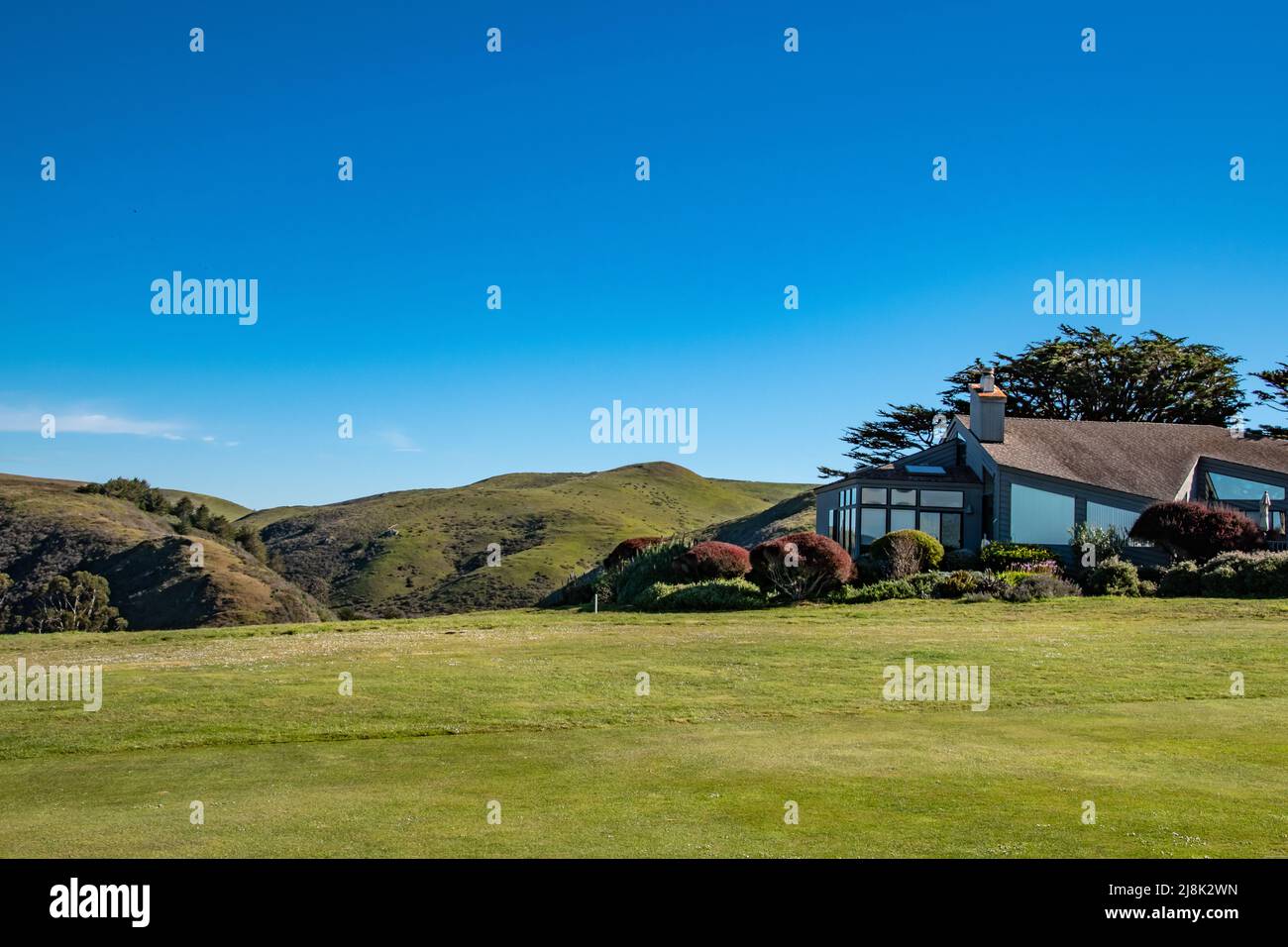 Verdi colline ondulate circondano una casa molto geometrica sotto grandi cieli blu. Lungo la comunità dei campi da golf a Bodega Bay, California. Foto Stock