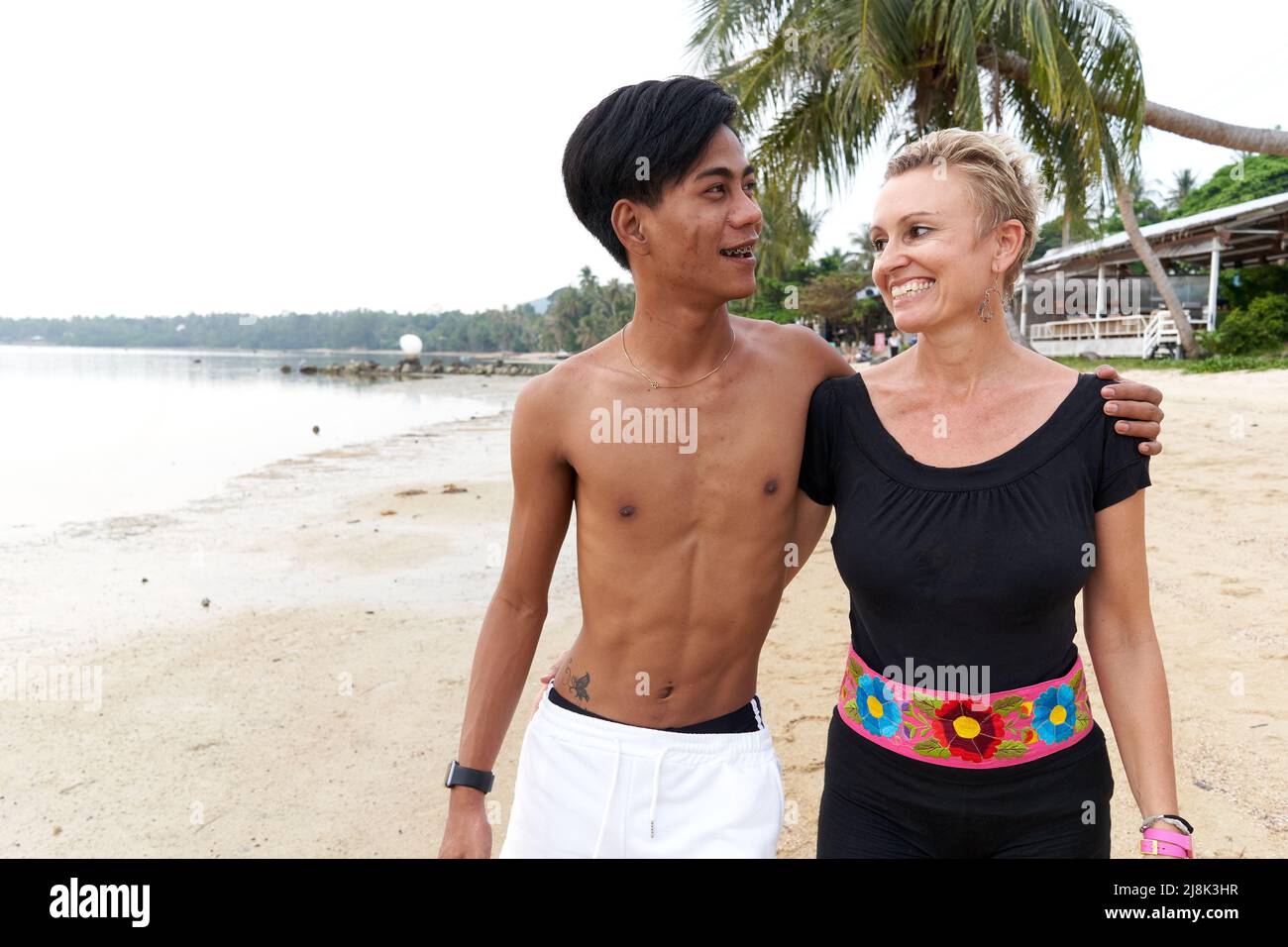 Sorridente coppia multiculturale che cammina lungo una spiaggia tropicale Foto Stock