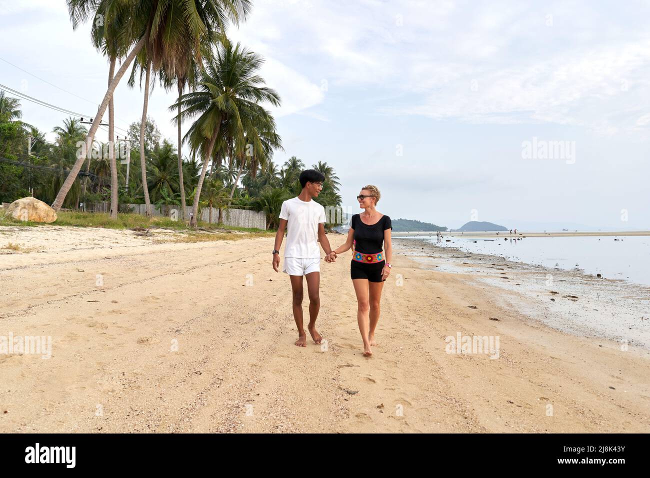 Coppia multietnica camminando insieme in una spiaggia di sabbia tropicale Foto Stock