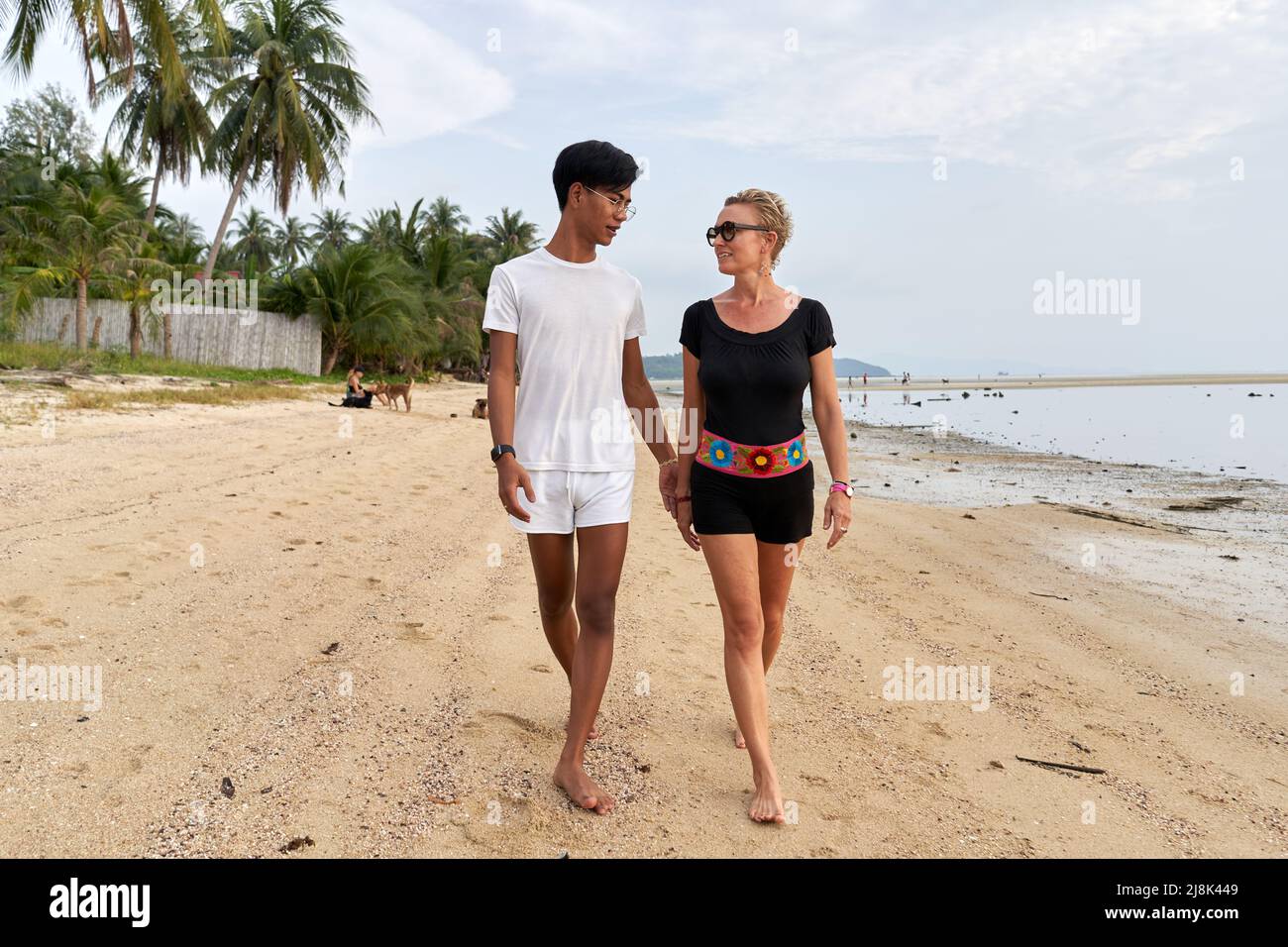 Coppia multiculturale che cammina lungo una spiaggia paradisiaca che tiene le mani Foto Stock