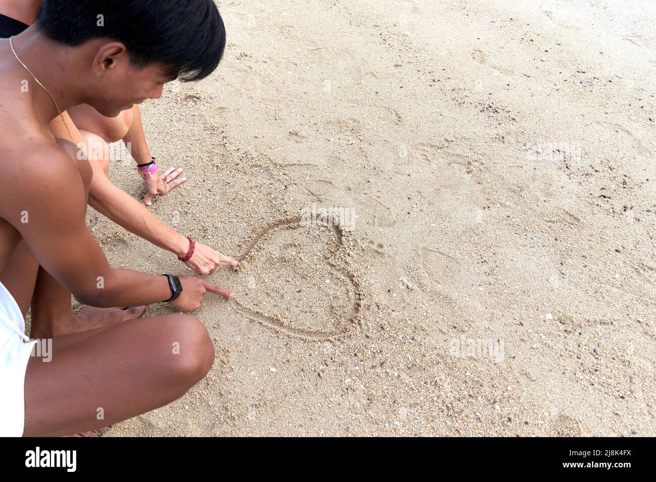 Coppia multiculturale che attingendo un cuore sulla sabbia sulla spiaggia Foto Stock