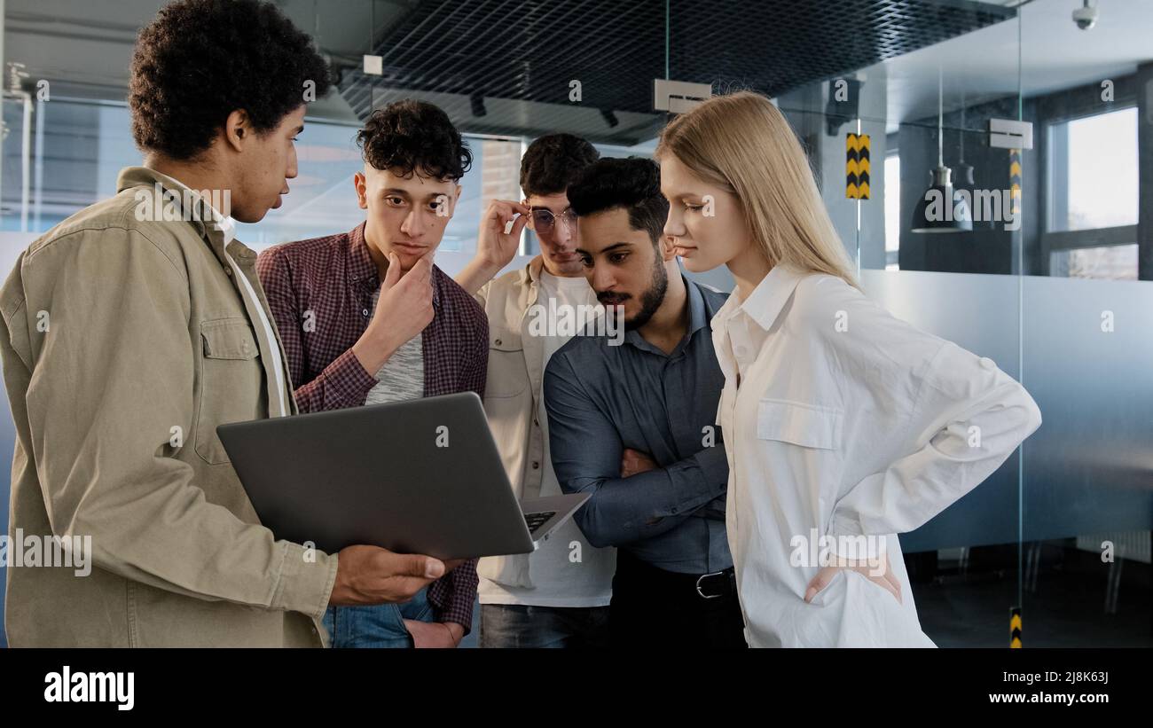 Il giovane dipendente dell'azienda spiega la strategia di sviluppo racconta nuove idee mostrando il piano di lavoro sul notebook a un team creativo sorridente e diversificato Foto Stock