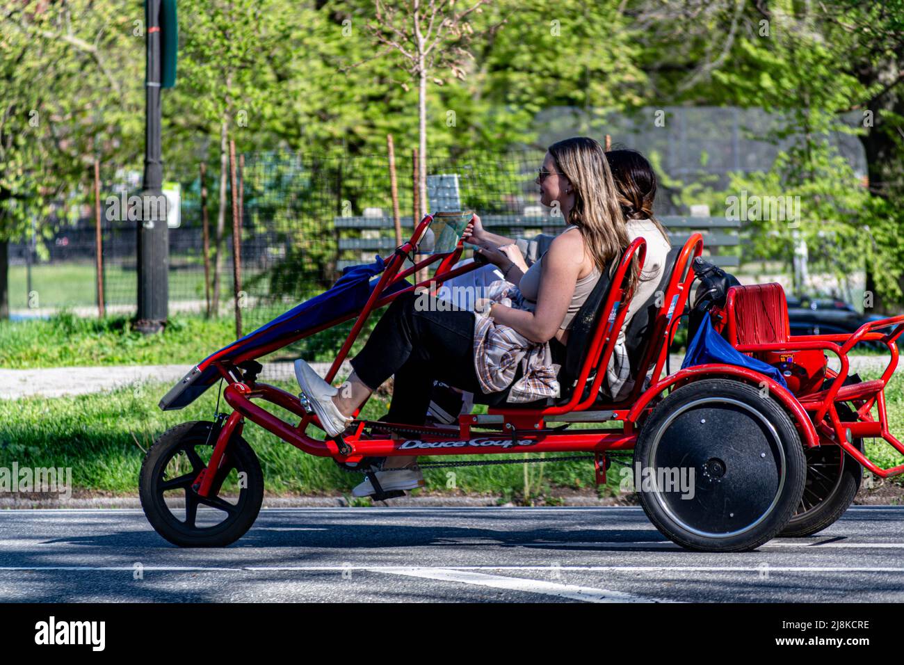 Due giovani donne che pedalano un triciclo affittato nel Prospect Park nella primavera del 2022 Foto Stock